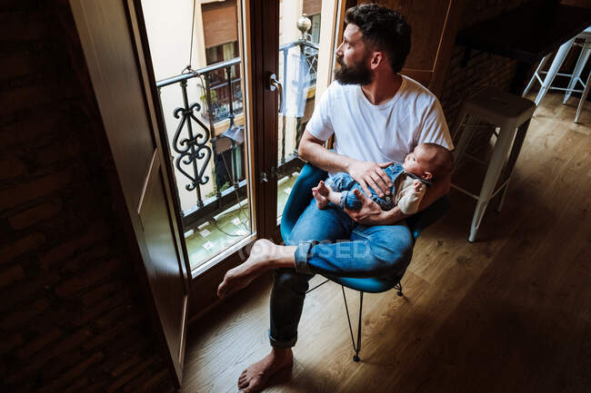 Père barbu avec bébé assis près de la fenêtre — Photo de stock