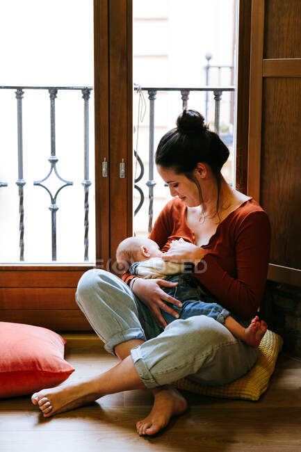 Щаслива мати грудного вигодовування дитини біля вікна — стокове фото