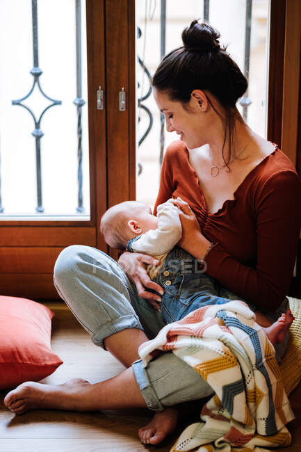 Feliz madre amamantando bebé cerca de ventana - foto de stock