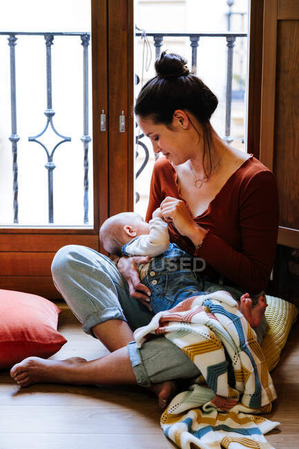 Щаслива мати грудного вигодовування дитини біля вікна — стокове фото