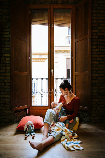 Feliz madre amamantando bebé cerca de ventana - foto de stock