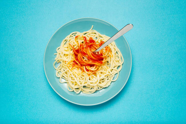 Top view of blue ceramic plate with pasta and tomato sauce on light blue background — Stock Photo