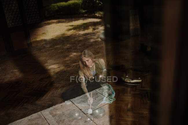 Зверху жінка сидить на підлозі за склом і грає у величезні миски в затишній кімнаті вдома — стокове фото