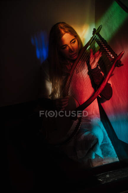 Desde arriba mujer tocando música tradicional en lira mientras está sentado en la habitación con iluminación multicolor - foto de stock