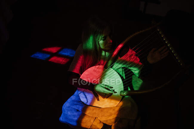 Жінка грає в ліру під барвистим світлом — стокове фото