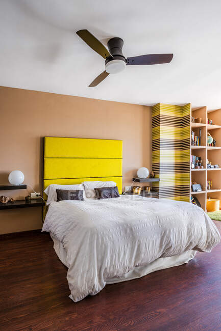 Cómoda cama con cabecero amarillo brillante en moderno apartamento estudio decorado en estilo minimalista - foto de stock