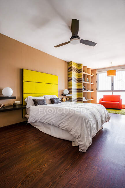 Komfortables Bett mit leuchtend gelbem Kopfteil in modernem Studio-Apartment im minimalistischen Stil eingerichtet — Stockfoto