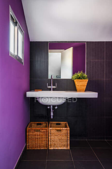 Современная ванная комната с красочной фиолетовой стеной с большим зеркалом, расположенная над стильной белой раковиной с соломенными корзинами — стоковое фото