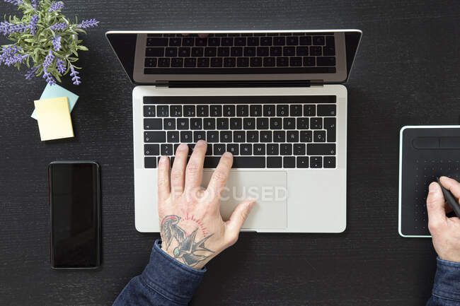 Von oben anonymer Mann tippt auf Laptop-Tastatur, während er am Tisch sitzt und zu Hause während der Quarantäne an einem Projekt arbeitet — Stockfoto