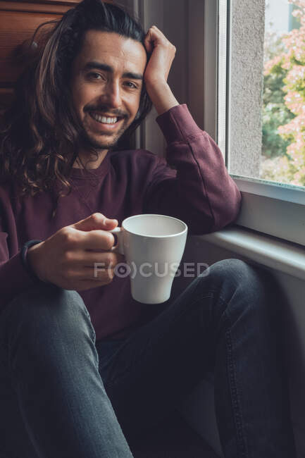 Дорослий чоловік з чашкою, що дивиться у вікно — стокове фото