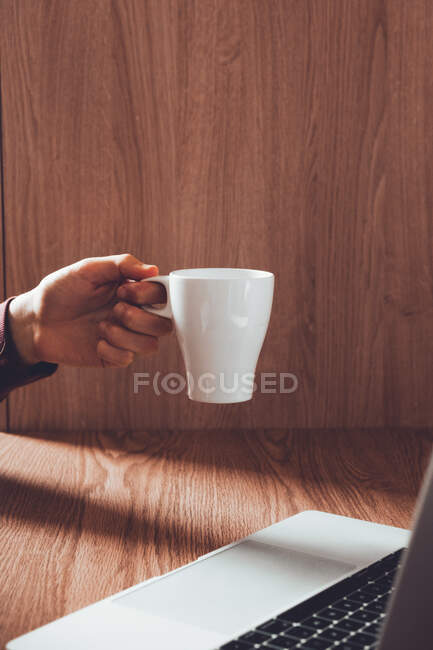 Crop man with mug using laptop — Stock Photo