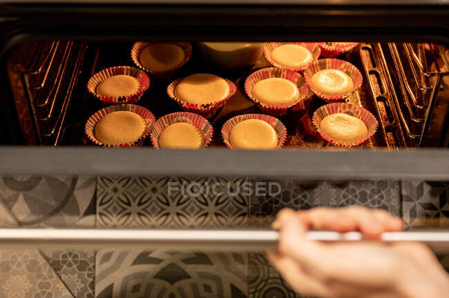 Von oben anonyme Person öffnet heißen Ofen und überprüft Cupcakes während der Zubereitung von Gebäck zu Hause — Stockfoto