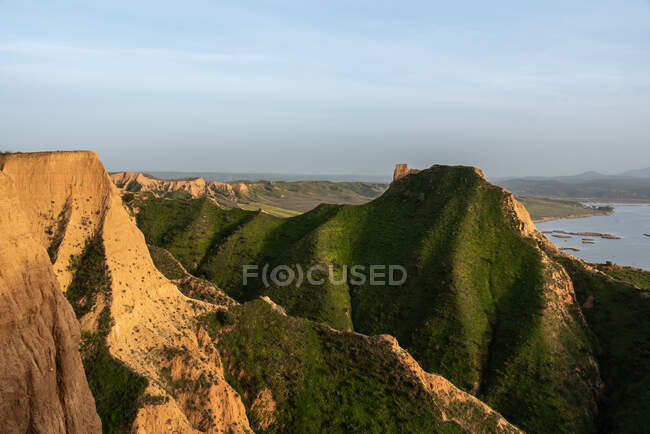Verde collina erbosa in una natura tranquilla vicino antiche rovine torre con paesaggio lacustre sullo sfondo — Foto stock