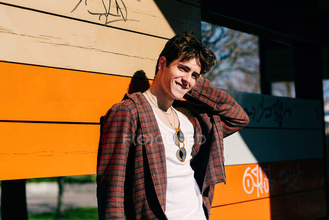 Handsome male standing looking at camera on sunny day on leaning on a wooden colorful wall in the city street — Stock Photo