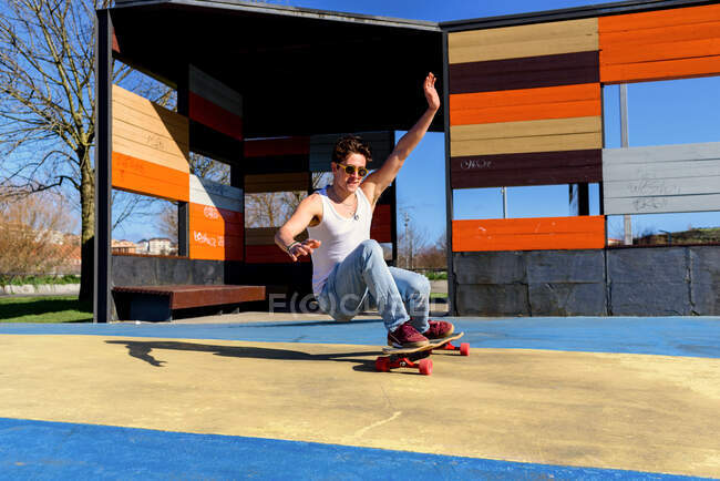 Junge hübsche Männchen mit erhobenen Armen fallen vom Skateboard beim Trickversuch an sonnigen Tagen auf dem Sportplatz — Stockfoto