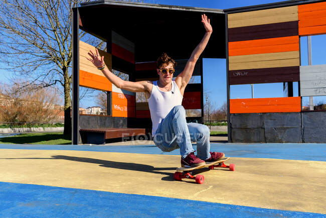 Young handsome male with raised arms falling from skateboard while trying to do trick on sunny day on sports ground — Stock Photo