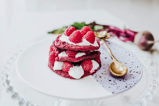 High angle of delicious organic beet pancakes with fresh raspberry on plate with golden spoon on white table — Stock Photo