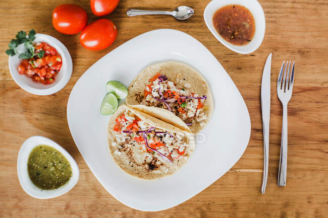 Deliziosi tacos messicani con ripieno di verdure serviti con fette di lime verde sul piatto sul tavolo — Foto stock