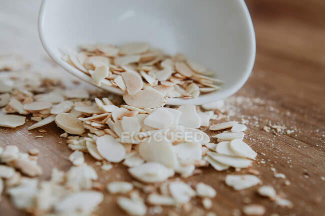 Bowl of almond chips spilled on wooden table — Stock Photo