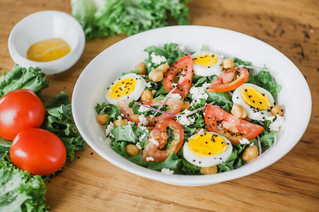 Bowl of tomato and lettuce salad with chickpeas and boiled eggs placed on table — Stock Photo
