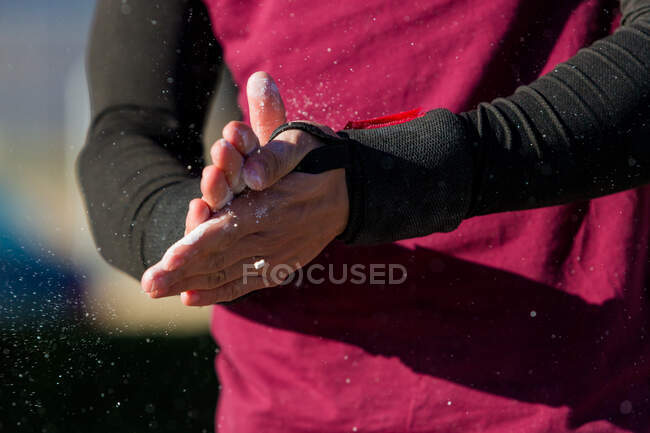Atleta masculino irreconhecível no sportswear esfregando as mãos cobertas com pó durante o treino no dia ensolarado — Fotografia de Stock