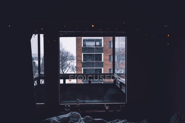 Edificio de apartamentos situado en la calle nevada detrás de balcón y ventana de acogedora habitación oscura - foto de stock