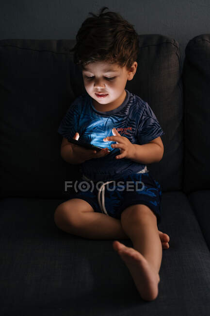 Curioso menino navegando smartphone em casa — Fotografia de Stock
