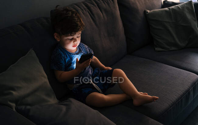 Curioso menino navegando smartphone em casa — Fotografia de Stock