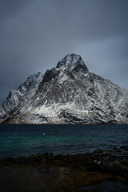 Vue à couper le souffle de l'eau de mer bleu ondulé contre les crêtes de montagne enneigées sur le rivage sous un ciel gris nuageux en hiver en Norvège — Photo de stock