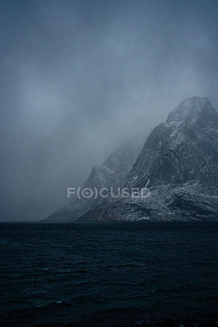 Breathtaking view of blue rippled sea water against snowy mountain ridges on shore under gray cloudy sky in wintertime in Norway — Stock Photo