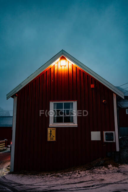 Dark red striped cottage with white windows and snowy roof in small town in overcast weather in Lofoten — Stock Photo