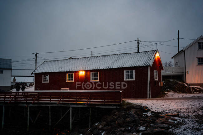 Chalet à rayures rouge foncé avec fenêtres blanches et toit enneigé dans une petite ville par temps couvert à Lofoten — Photo de stock