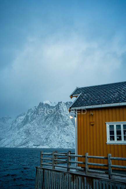 Gelbe Landhäuser an der Küste der Meerenge gegen neblige schneebedeckte Bergkämme bei bewölktem Wetter in Norwegen — Stockfoto