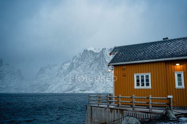 Case di campagna gialle sulla costa dello stretto contro creste nevose nebbiose in tempo nuvoloso in Norvegia — Foto stock