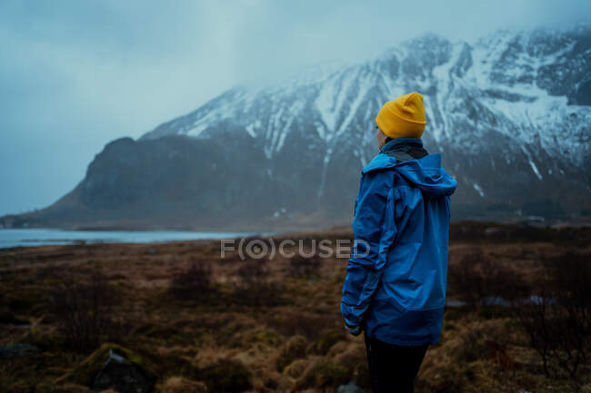 Visão traseira da mulher pensativa calma em roupas quentes desfrutando de paisagens enquanto está sozinho contra a montanha nebulosa nevada na Noruega — Fotografia de Stock