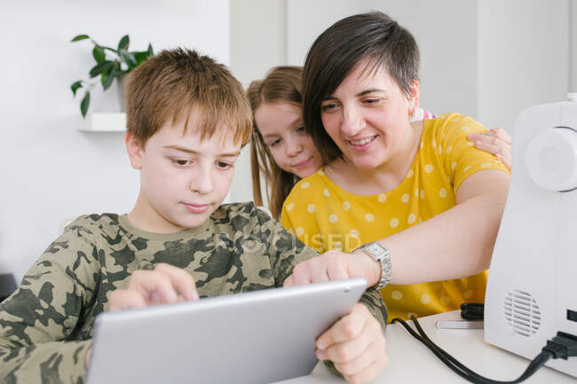Mulher adulta e crianças navegando tablet moderno juntos enquanto sentados à mesa em casa — Fotografia de Stock
