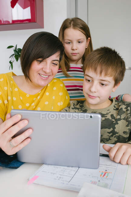 Доросла жінка і діти переглядають сучасний планшет разом, сидячи за столом вдома — стокове фото