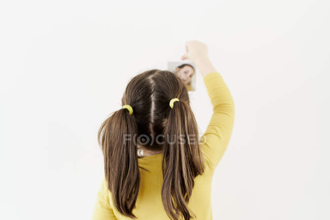 Linda niña en un vestido amarillo está de pie sobre su espalda colocando fotos de sí misma mostrando varias emociones - foto de stock