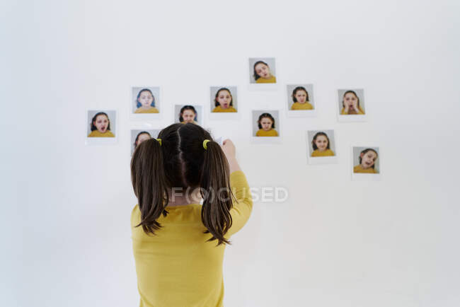Petite fille mignonne dans une robe jaune est debout sur son dos plaçant des photos d'elle-même montrant diverses émotions — Photo de stock