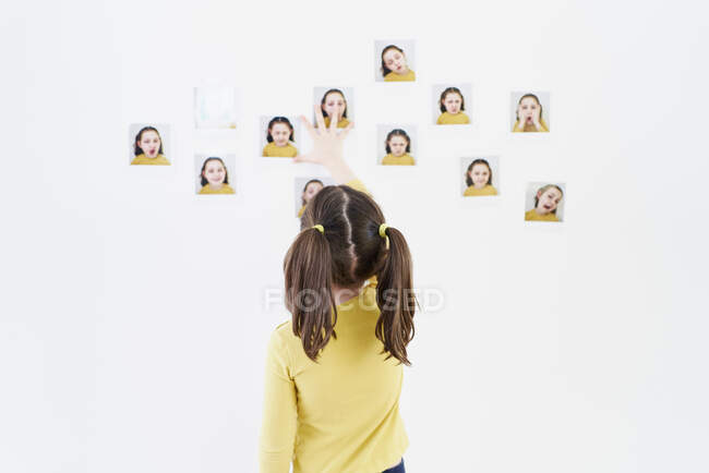 Cute little girl in a yellow dress is standing on her back placing photos of herself showing various emotions — Stock Photo