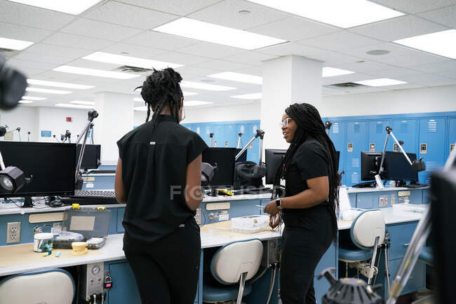 Афроамериканские женщины с косичками и дредами, стоящие рядом со столом и разговаривающие друг с другом во время совместной работы в лаборатории — стоковое фото