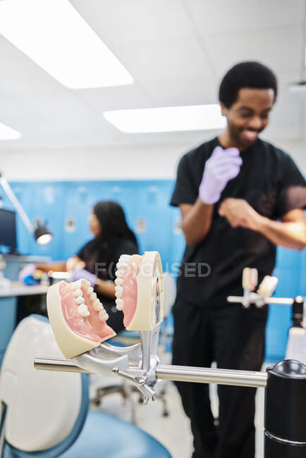 False teeth attached to metal occludator on blurred background of modern orthodontic lab and ethnic staff — Stock Photo