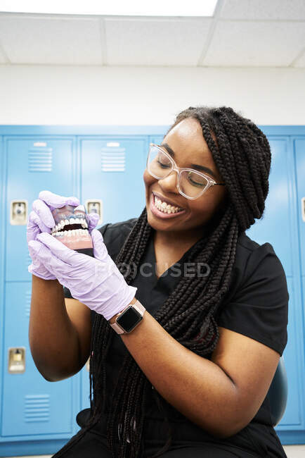 Happy black dental technician with braids showing false teeth while working in contemporary laboratory — Stock Photo