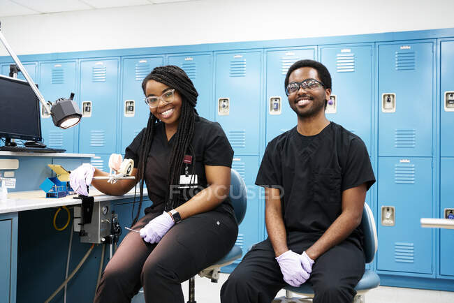 Mulher afro-americana feliz com tranças e homem barbudo preto sorrindo e olhando para a câmera enquanto cria dentaduras em laboratório moderno — Fotografia de Stock