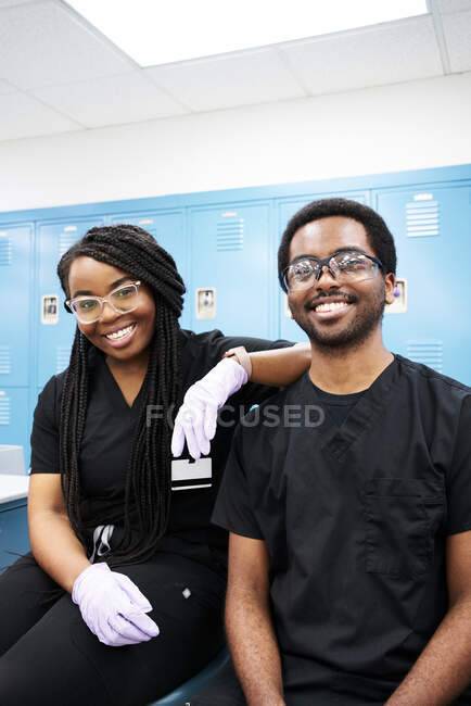 Mujer afroamericana feliz con trenzas y hombre barbudo negro sonriendo y mirando a la cámara mientras crea dentaduras postizas en el laboratorio moderno - foto de stock