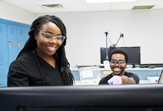 Mulheres negras e homem de uniforme discutindo dados sobre computador enquanto trabalham em laboratório contemporâneo juntos — Fotografia de Stock