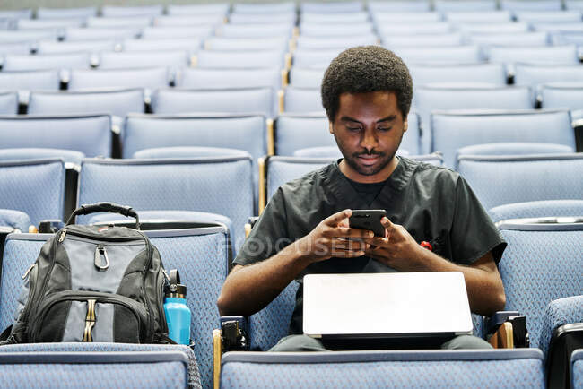 Schwarzer Mann sitzt im Hörsaal und surft während des Unterrichts im Hörsaal mit Smartphones — Stockfoto