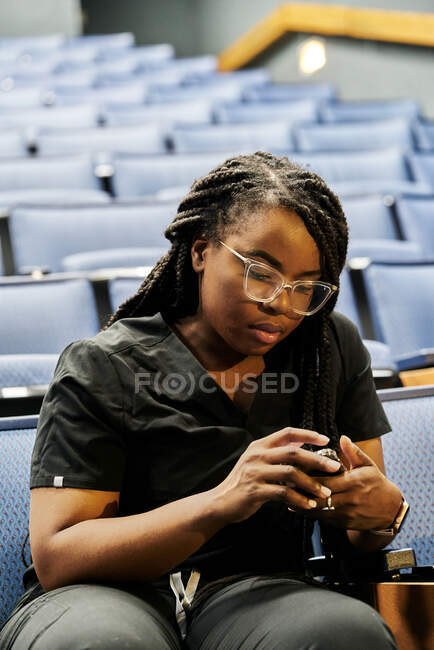 Black woman sitting in auditorium and browsing smartphones during lesson in auditorium — Stock Photo