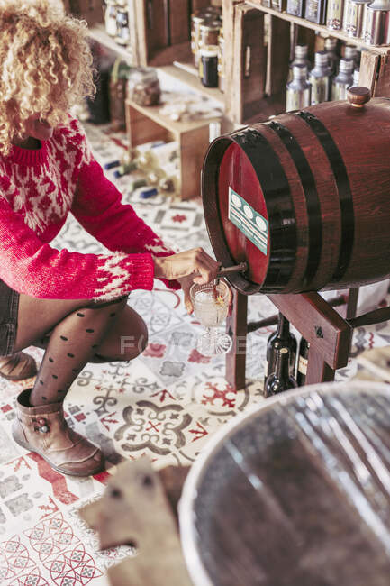 Зверху анонімний продавець наповнює скляну чашку вином з бочки під час роботи в місцевому продуктовому магазині — стокове фото