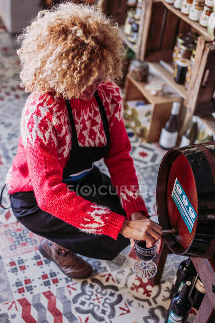 From above anonymous seller filling glass cup with wine from barrel while working in local food store — Stock Photo